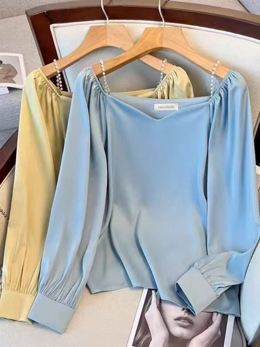 satin blouse, perfect for a vintage or office-casual Korean-inspired look, features a V-neckline with delicate pearl detailing at the shoulders and stylish gathered or ruffled long sleeves.