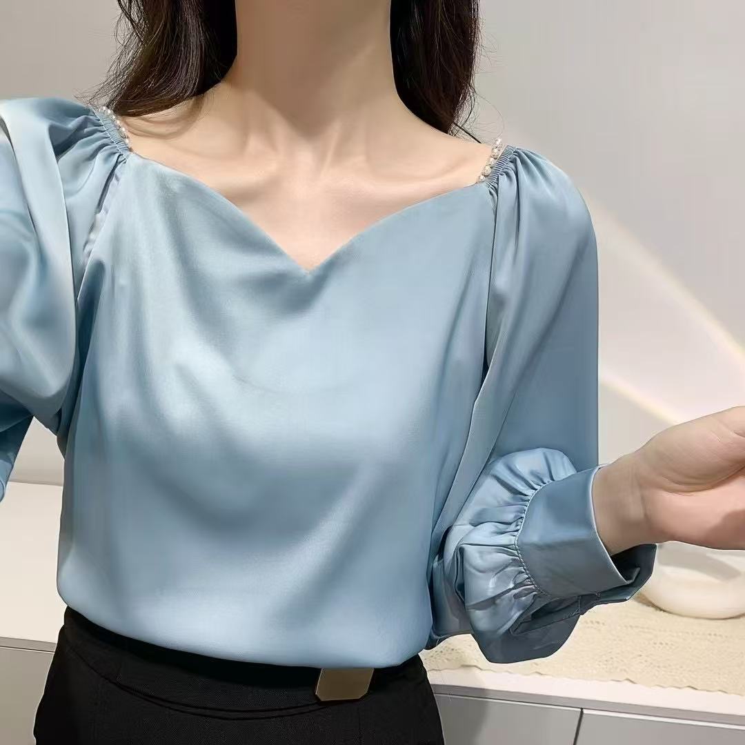 satin blouse, perfect for a vintage or office-casual Korean-inspired look, features a V-neckline with delicate pearl detailing at the shoulders and stylish gathered or ruffled long sleeves.