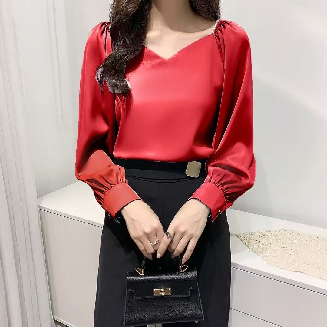 satin blouse, perfect for a vintage or office-casual Korean-inspired look, features a V-neckline with delicate pearl detailing at the shoulders and stylish gathered or ruffled long sleeves.